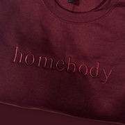 Maroon sweatshirt with 'homebody' text on a dark red background