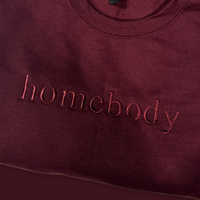 Maroon sweatshirt with 'homebody' text on a dark red background